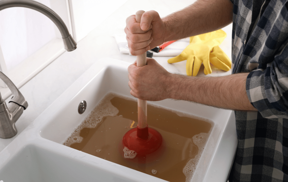 man unblocking drain with plunger